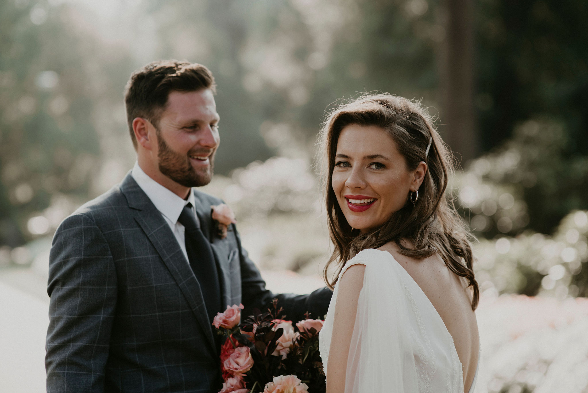 Bride looks back at the camera smiling while groom looks lovingly at her sun drenched in the Fitzroy Gardens Melbourne Elopement and Wedding Photography Sarah Matler Photographer